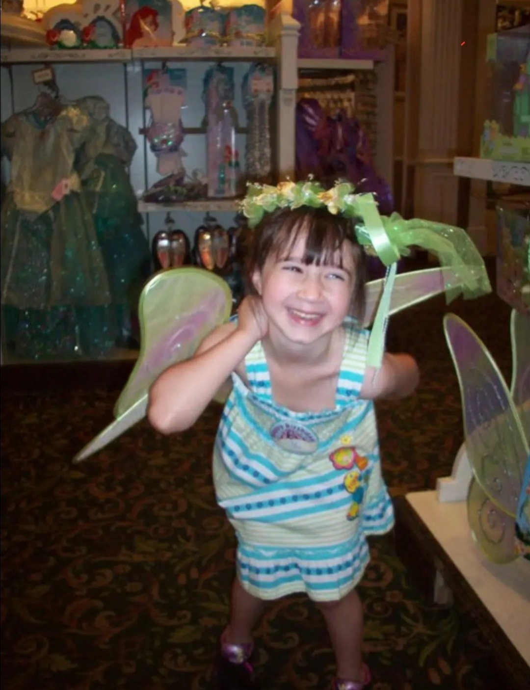 A young girl wearing a flower crown, striped dress, and fairy wings